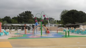 A water play area with a rainbow arch, water jets, and green and white plastic chairs. - Spacious, comfortable mobile home for 6/8 people (40m2) (Les Mathes)