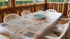 A covered outdoor dining area with a table set for two, surrounded by white plastic chairs. - Spacious, comfortable mobile home for 6/8 people (40m2) (Les Mathes)