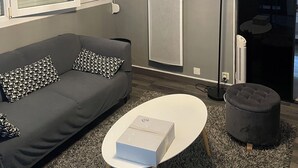 Un salon moderne avec un canapé gris, une table basse blanche, une horloge et un radiateur.