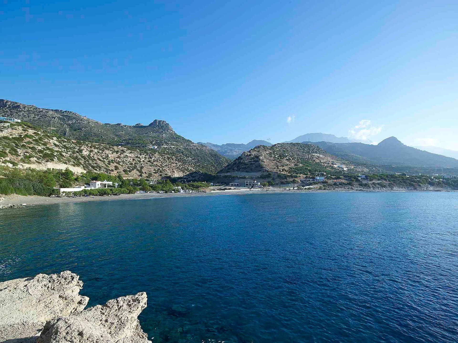 Un paisaje costero con terreno rocoso y un mar azul cristalino.