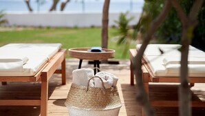 A wooden deck with two sun loungers, a woven basket, and a small round table. - Beach Villa in Crete - Villa Kirvas (Ierapetra)