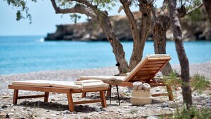 A beachside setting with wooden lounge chairs and a woven basket, likely for beachgoers. - Beach Villa in Crete - Villa Kirvas (Ierapetra)