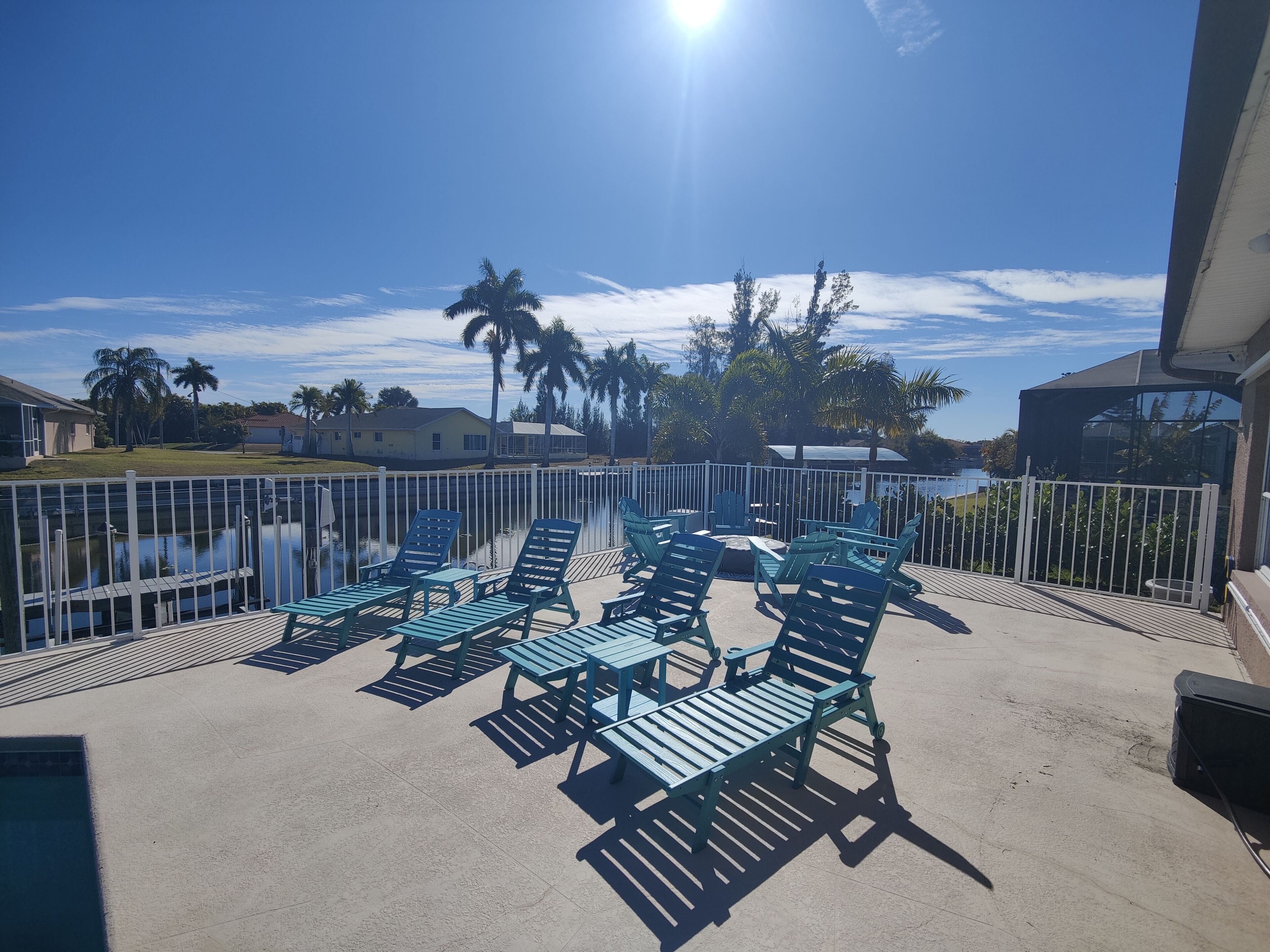 A balcony with blue chairs and a table, overlooking a body of water and palm trees.