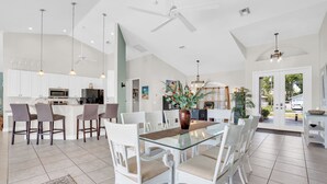 A spacious kitchen with white cabinets, a central island, and a dining area with white chairs and a glass table. - Villa Coconut Cove - Beautiful waterfront home w. heated pool (Cape Coral)