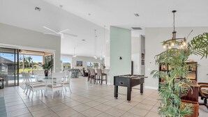 A spacious living area with a foosball table, a dining table with chairs, and a large window overlooking a pool. - Villa Coconut Cove - Beautiful waterfront home w. heated pool (Cape Coral)
