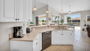 A modern kitchen with white cabinets, a dishwasher, a coffee maker, and pendant lights. - Villa Coconut Cove - Beautiful waterfront home w. heated pool (Cape Coral)