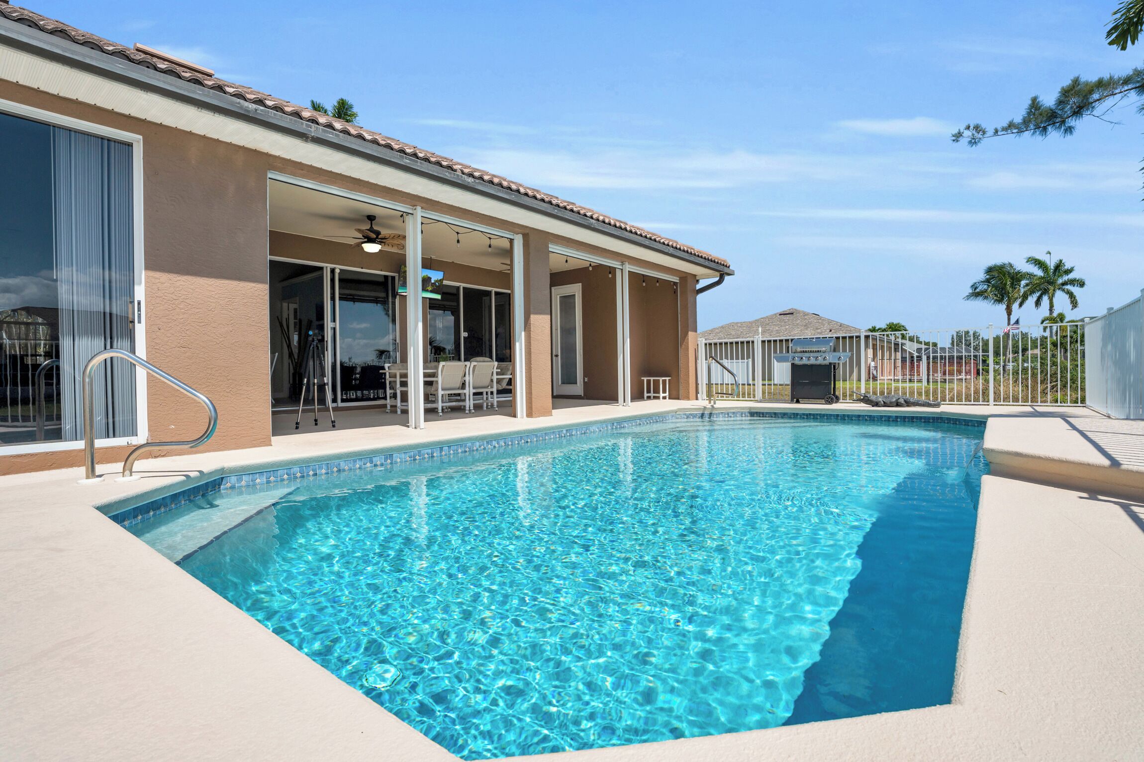 A swimming pool with a clear blue water, a covered patio area, and a building with large windows and a door.