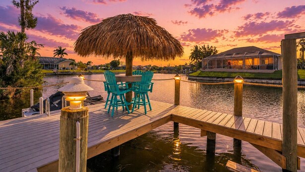 A wooden dock with a thatched umbrella, teal chairs, and a table. - Villa Coconut Cove - Beautiful waterfront home w. heated pool (Cape Coral)
