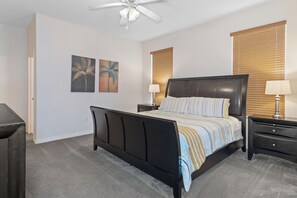 Een slaapkamer met een zwart bed, twee nachtkastjes, een plafondventilator en een raam met jaloezieën.