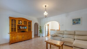 Ein Wohnzimmer mit einem Holzkabinett, einem beige farbenen Sofa, einem Holztisch und einer Pendelleuchte.