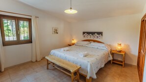 Ein Schlafzimmer mit einem Bett, zwei Nachttischen, einer Bank und einem Fenster mit Vorhängen.