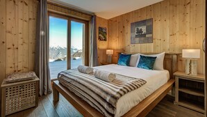 A wooden-paneled bedroom with a large bed, two bedside lamps, a nightstand, and a view of mountains through a sliding door. - Chalet Gentiane - La Tzoumaz, 4 Vallees (La Tzoumaz)