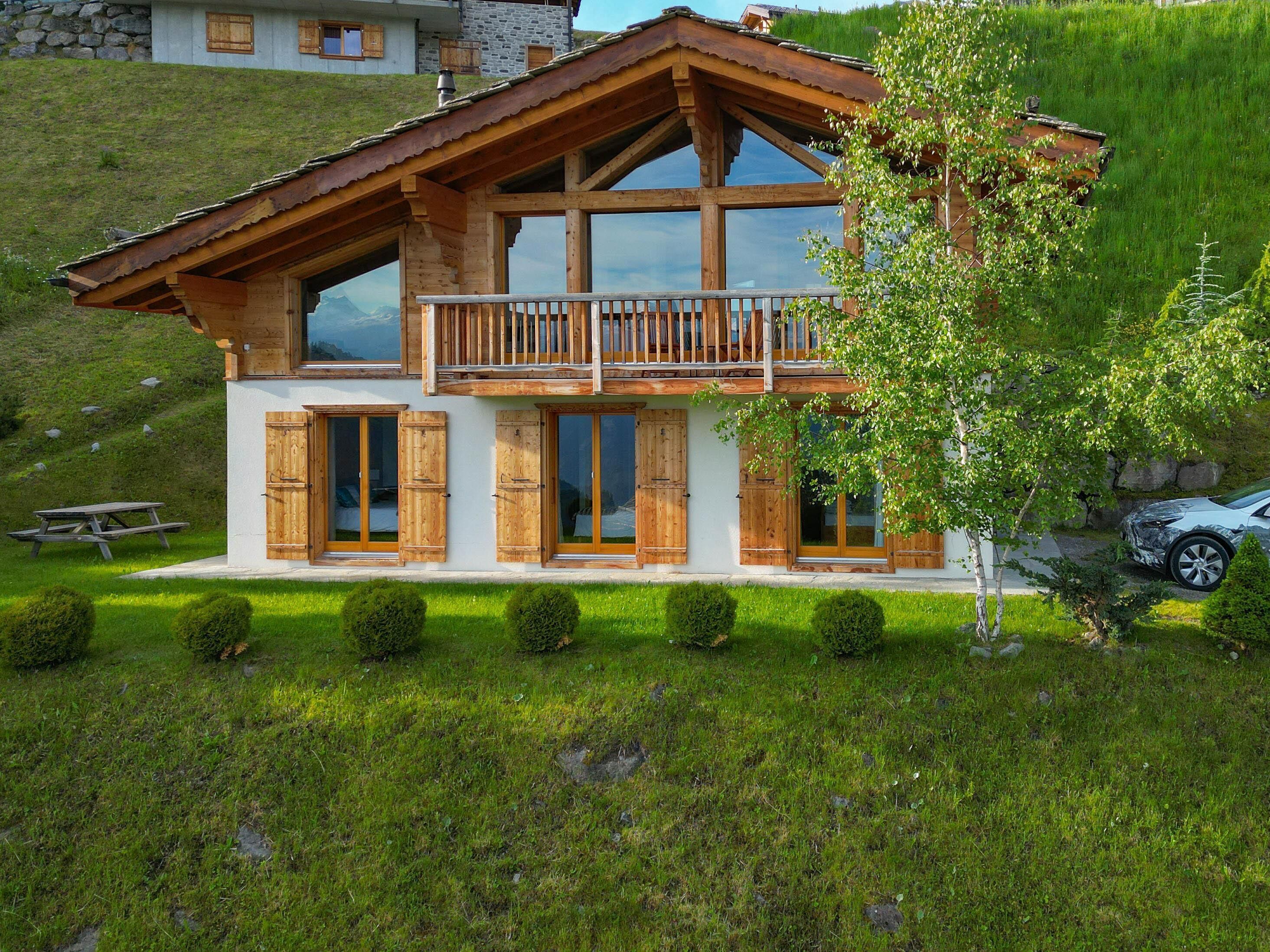 Un chalet doté d’un balcon en bois, de grandes fenêtres et d’un mur de pierre en arrière-plan.