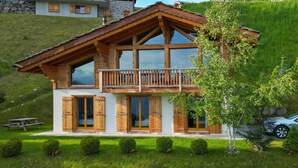 A chalet with a wooden balcony, large windows, and a stone wall in the background. - Chalet Gentiane - La Tzoumaz, 4 Vallees (La Tzoumaz)