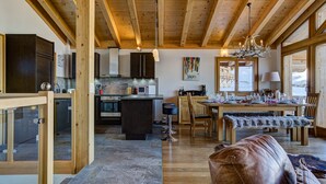 A spacious kitchen with wooden beams, a dining area with a table set for four, and a cozy seating area with a leather ottoman. - Chalet Gentiane - La Tzoumaz, 4 Vallees (La Tzoumaz)