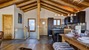 A spacious kitchen with wooden beams, a dining area with a wooden table set for four, and a large dog lying on a fur rug. - Chalet Gentiane - La Tzoumaz, 4 Vallees (La Tzoumaz)