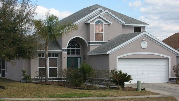 A two-story house with a garage, a large arched window, and a small front yard with landscaping. - Disney Quiet, Spacious, Contemporary / Salt Water Pool & Spa, Wi-fi (Davenport)
