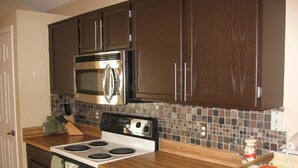 A kitchen with dark brown cabinets, a stainless steel microwave, a stove, and a tiled backsplash. - Disney Quiet, Spacious, Contemporary / Salt Water Pool & Spa, Wi-fi (Davenport)