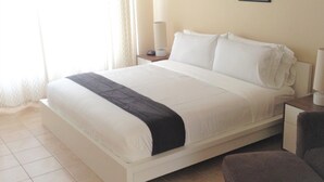 A neatly made bed with a white comforter and a dark blanket, a bedside table with a lamp, and a chair in a room with tiled flooring. - Disney Quiet, Spacious, Contemporary / Salt Water Pool & Spa, Wi-fi (Davenport)