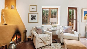 A cozy living room with a fireplace, two armchairs, a small table, and framed pictures on the wall. - Kiva Fireplace, Peaceful Luxury, Walk Everywhere (Santa Fe)