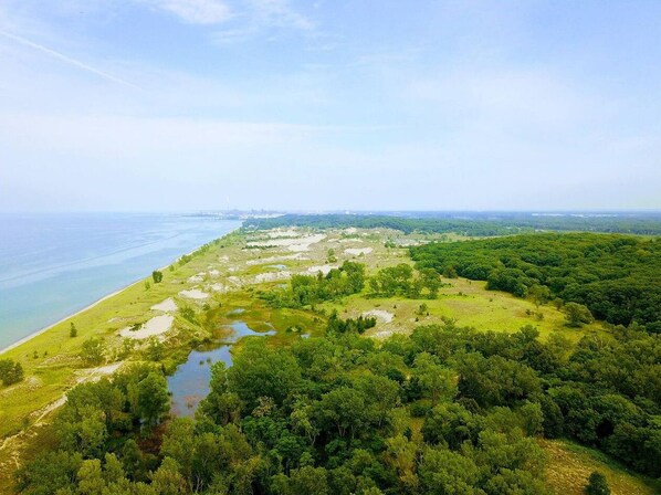 An aerial view of a coastal landscape with a mix of forested areas and open fields, a body of water, and a distant shoreline.