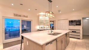 A modern kitchen with a large island, a built-in dishwasher, and a view of the beach through the sliding glass doors. - Skyline Views, Hot Tub, Beachfront, Lavish Kitchen at Dunetop Villa (Miller Beach)
