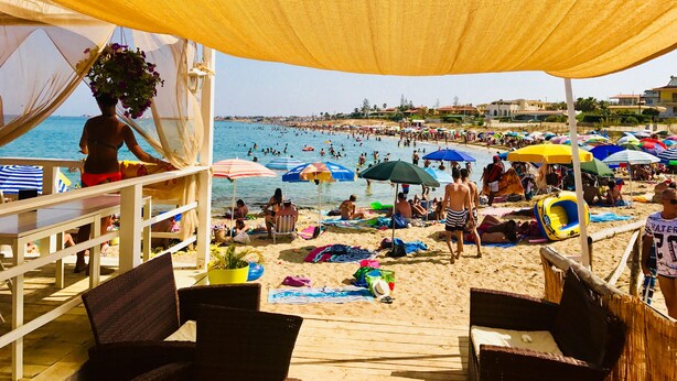 Une plage avec des parasols, des gens et une jetée.