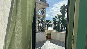 Un balcon doté d’un sol carrelé, d’une plante en pot et offrant une vue sur des palmiers et un ciel dégagé.