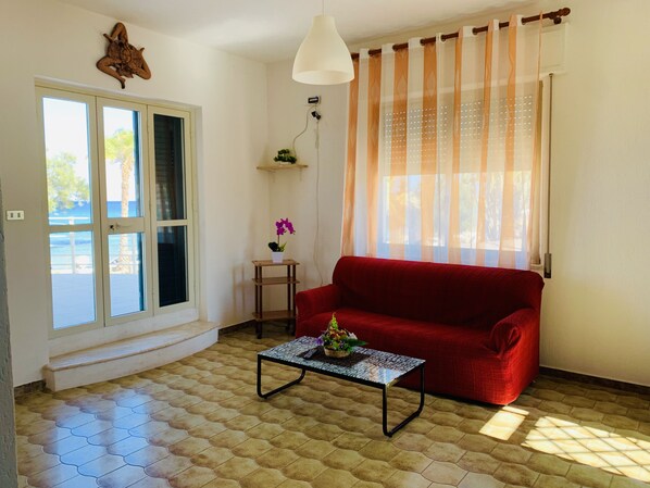 Ein Wohnzimmer mit einem roten Sofa, einem kleinen Tisch mit einer Pflanze, einer Pendelleuchte und einem Fenster mit Vorhängen.