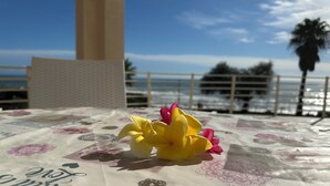 Une table recouverte d’une nappe à motifs floraux, avec une clé et une fleur jaune posées dessus, et en arrière-plan, une vue sur l’océan et des palmiers.