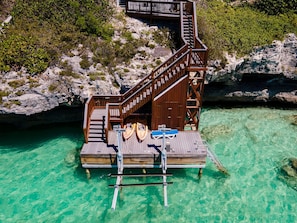 A wooden dock with a staircase leading to a deck, surrounded by clear turquoise water and rocky terrain. - Oceanfront Villa - Private Dock for Snorkeling, 3 mins to Private Beach (Providenciales)