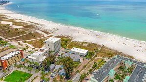 Vista aérea de un hotel frente al mar, con playa, estacionamiento y piscina.