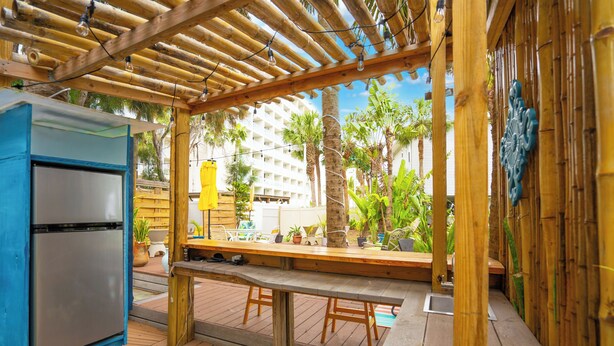 Un patio al aire libre con una pérgola de madera, un refrigerador de acero inoxidable y un banco de asiento.