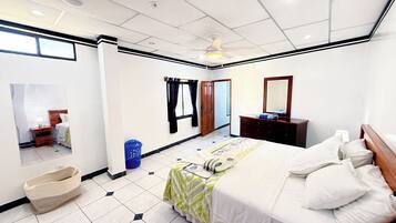 Une chambre d’hôtel avec un lit, une commode, un miroir, un ventilateur de plafond et une fenêtre.
