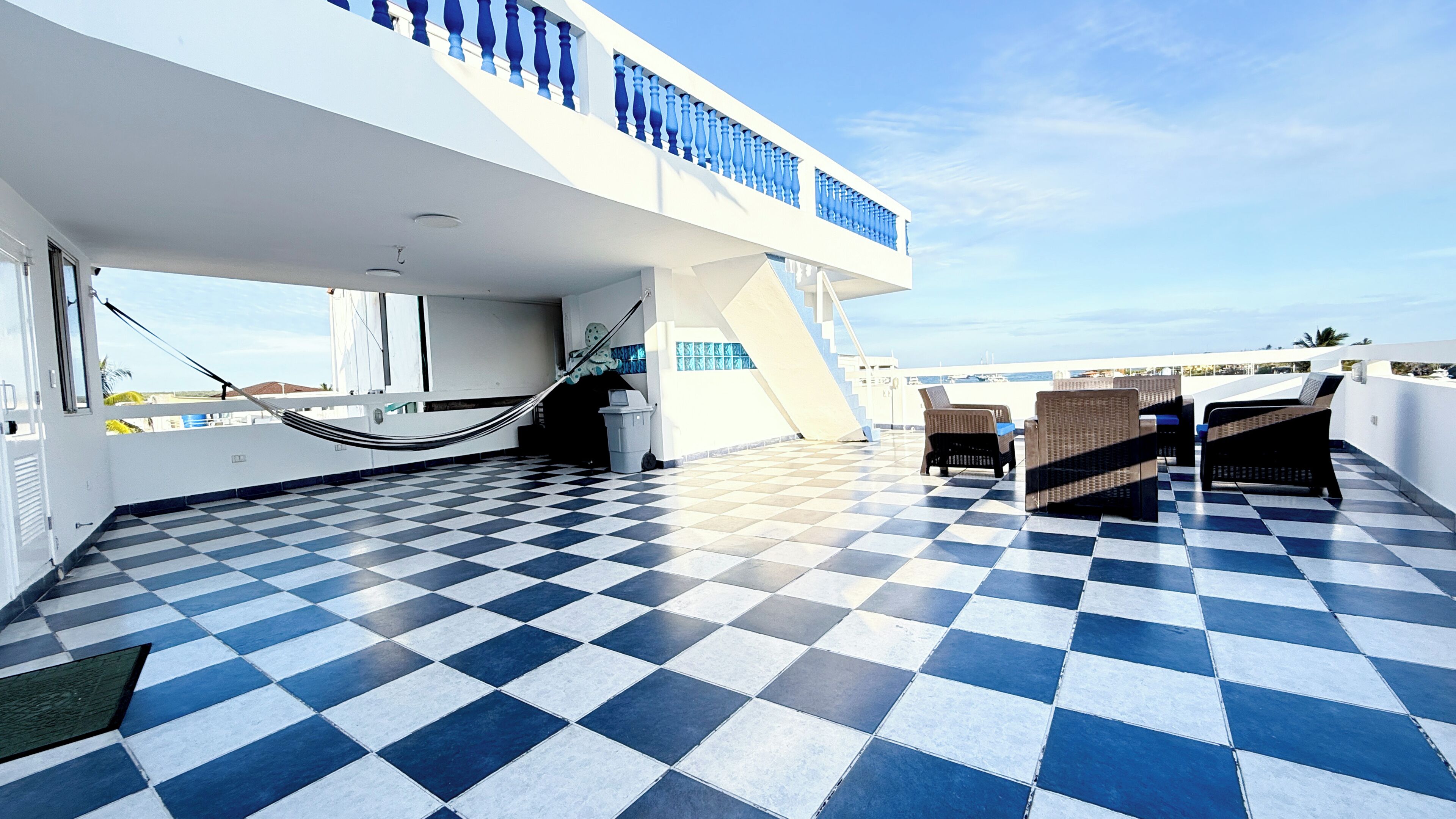 Une terrasse carrelée avec des meubles d’extérieur, un hamac et un escalier menant à un balcon doté d’une balustrade.