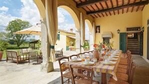 Un'area pranzo all'aperto con un lungo tavolo apparecchiato per la colazione, circondato da pilastri in pietra e ricoperto da un tetto in legno.