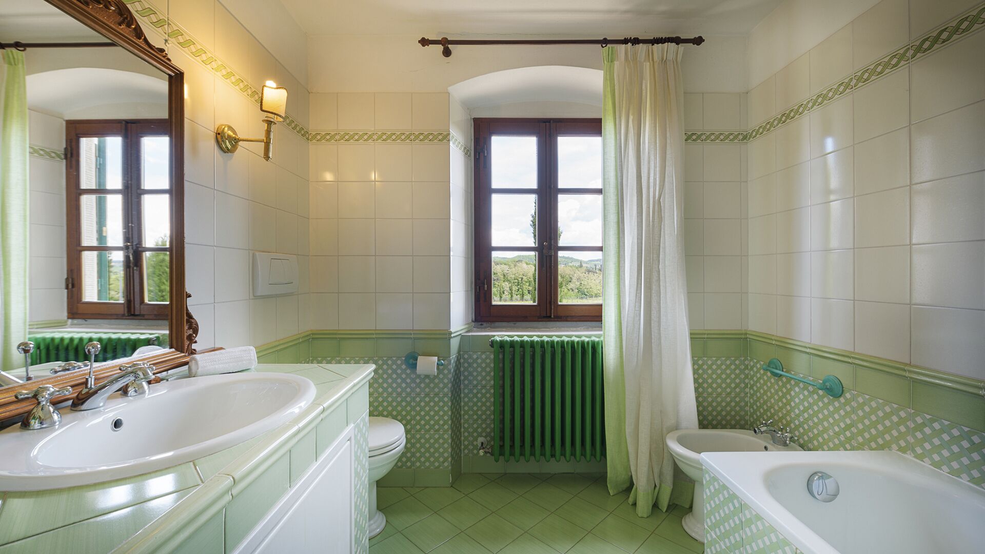 A bathroom with two sinks, a toilet, a bathtub, and a window with a view of greenery.