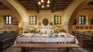 Una sala da pranzo con un lungo tavolo apparecchiato per un pasto, travi di legno al soffitto e quadri appesi alle pareti.