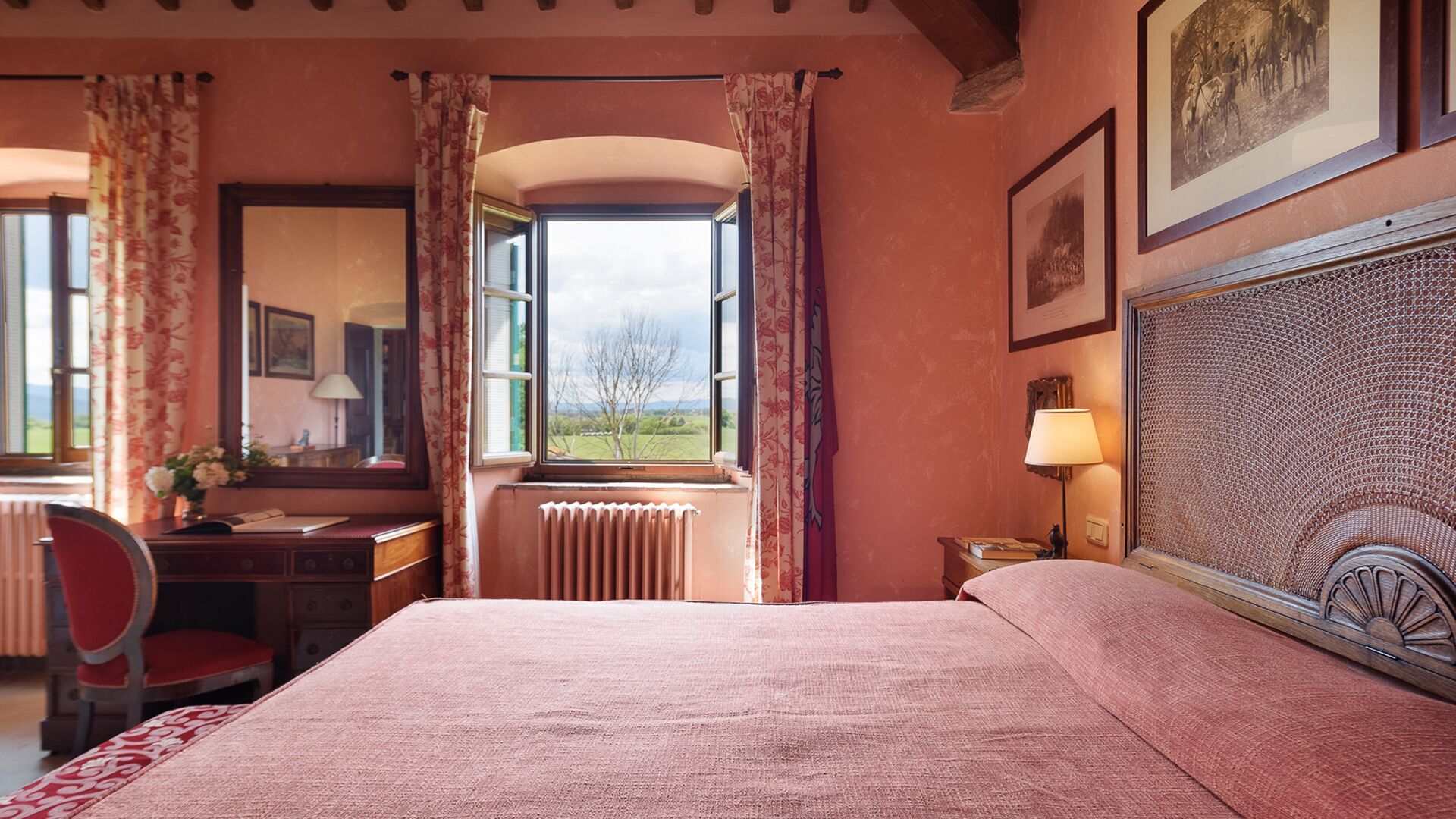 A bedroom with a large bed, a desk with a chair, a radiator, and a window with curtains.
