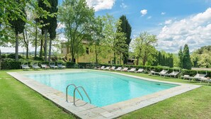 Una piscina rettangolare con una scaletta in metallo, circondata da un prato e alberi.