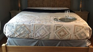 Una cama bien hecha con colcha estampada, dos lámparas de noche y una bandeja con vasos sobre la cama.