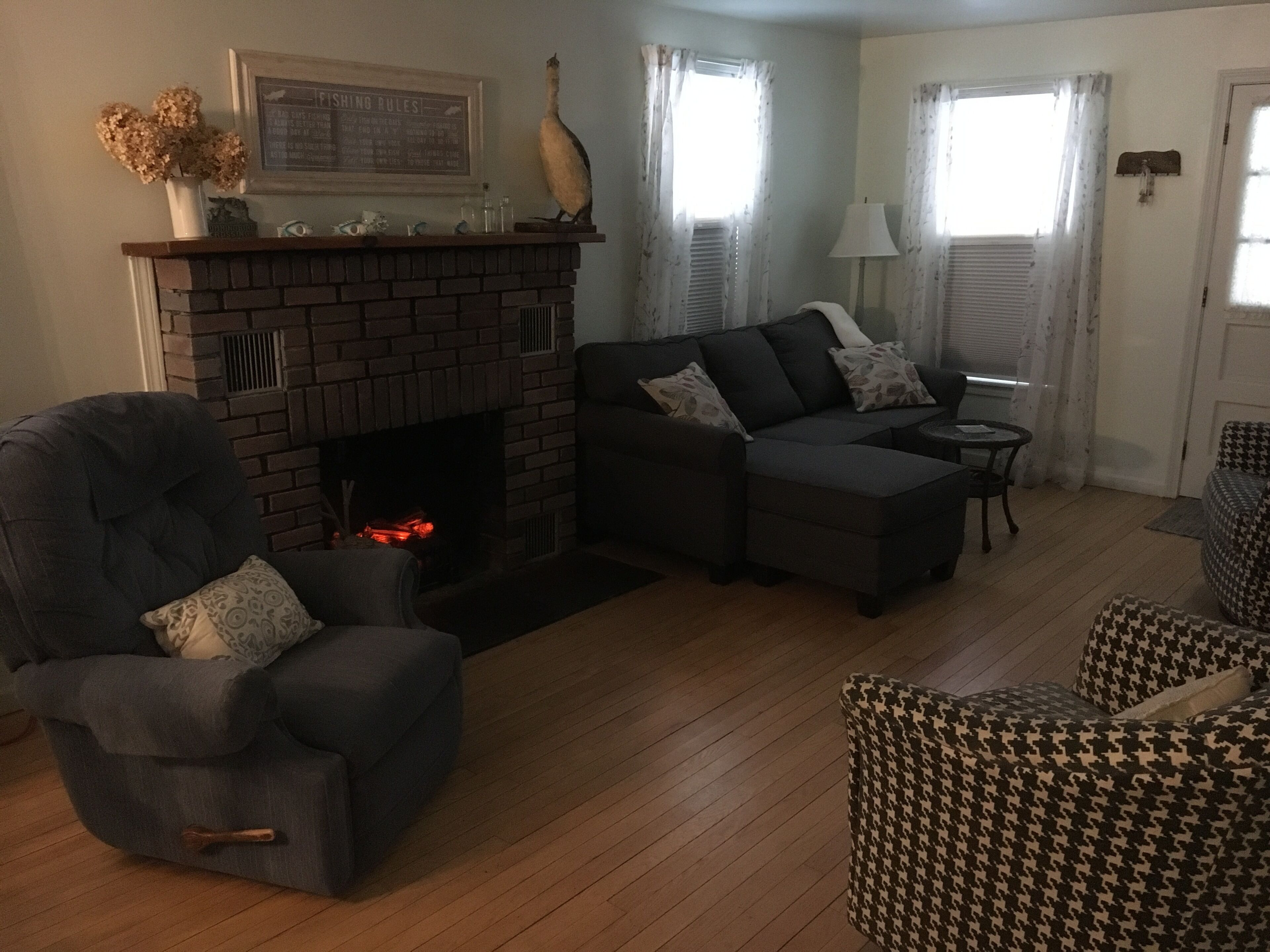Una sala de estar con chimenea de ladrillo, un sofá, una silla y un sillón a cuadros.