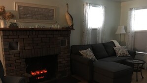 Una sala de estar con chimenea de ladrillo, un sofá, una mesita auxiliar y una lámpara.