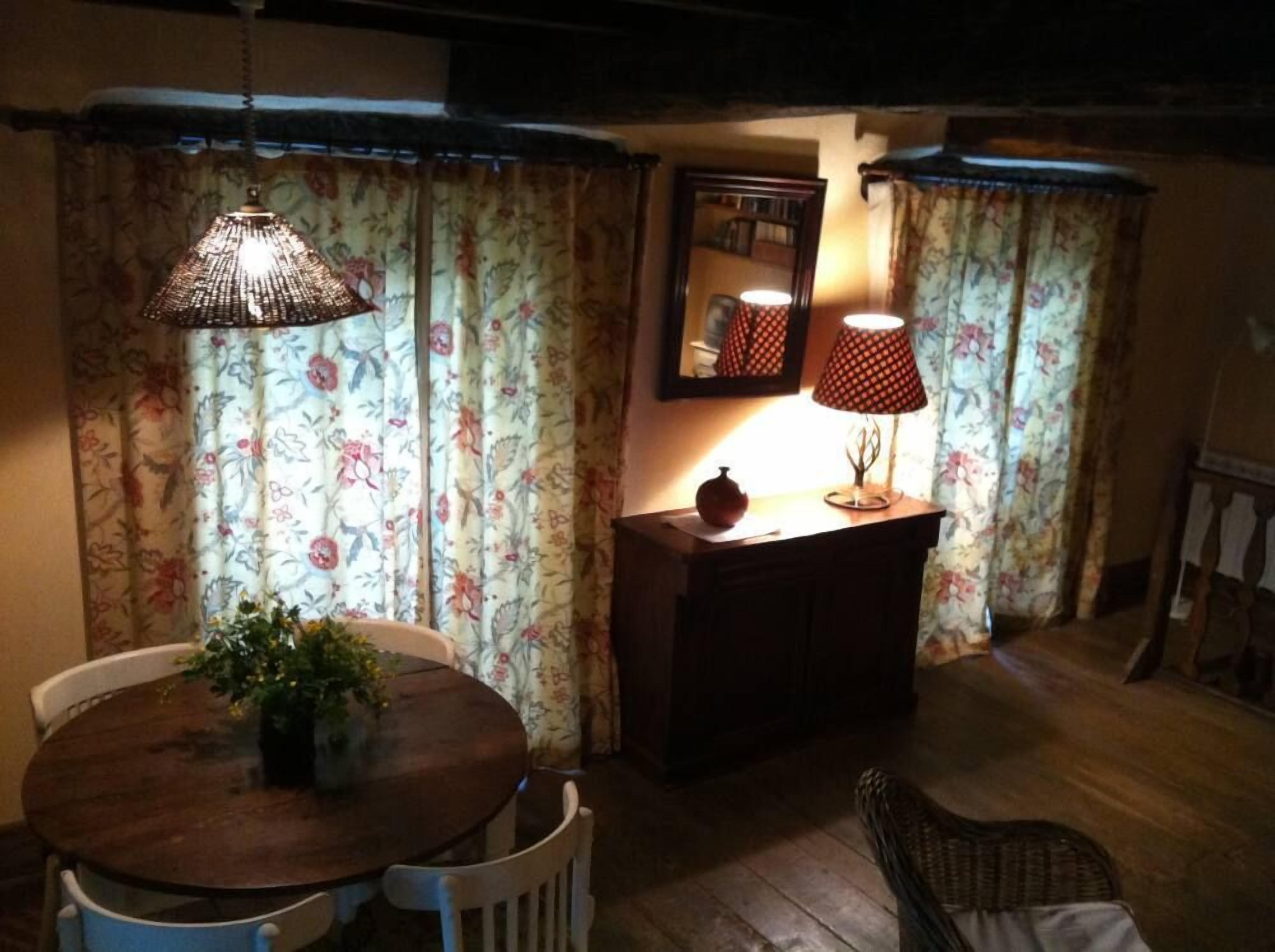 A cozy dining area with a wooden table and chairs, a hanging lamp, and a small side table with a lamp and a decorative item.