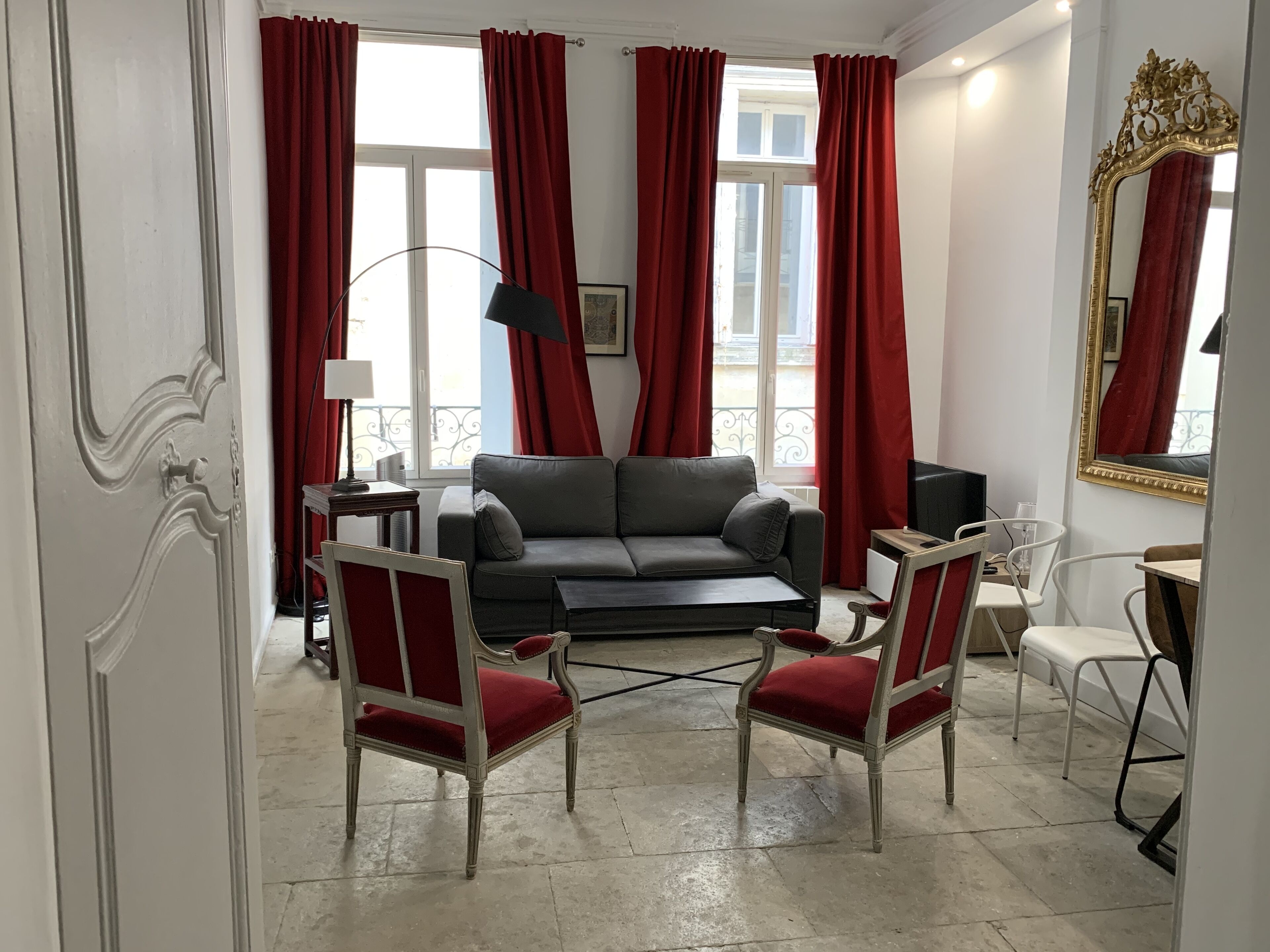 A living room with a grey sofa, two red upholstered chairs, a black floor lamp, and a large mirror with a gold frame.