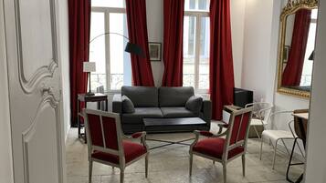 A living room with a grey sofa, two red upholstered chairs, a black floor lamp, and a large mirror with a gold frame.