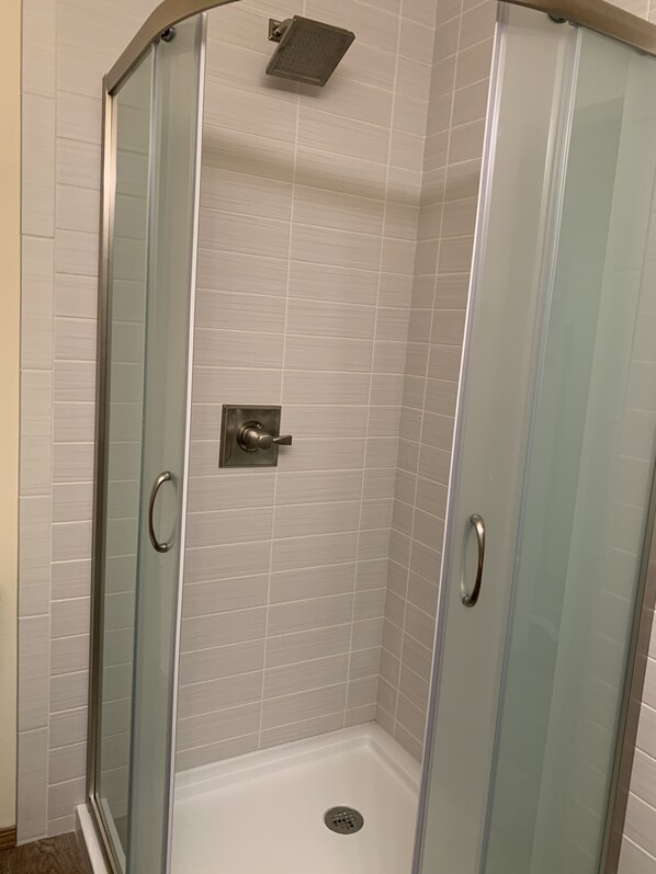 A glass-enclosed shower with a showerhead and a control panel.