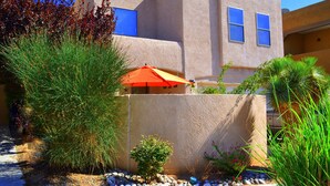 A modern building with a stucco exterior, a small patio area with a red umbrella, and various plants. -  SW STYLE/BREATHTAKING VIEWS & 8 Min. to OLD TWN~WOW REVIEWS/Long Term SPECIALS  (Albuquerque)