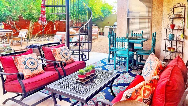 A patio area with a spiral staircase, outdoor seating with red and blue chairs, a table with a patterned table runner, and a decorative shelf with potted plants. -  SW STYLE/BREATHTAKING VIEWS & 8 Min. to OLD TWN~WOW REVIEWS/Long Term SPECIALS  (Albuquerque)