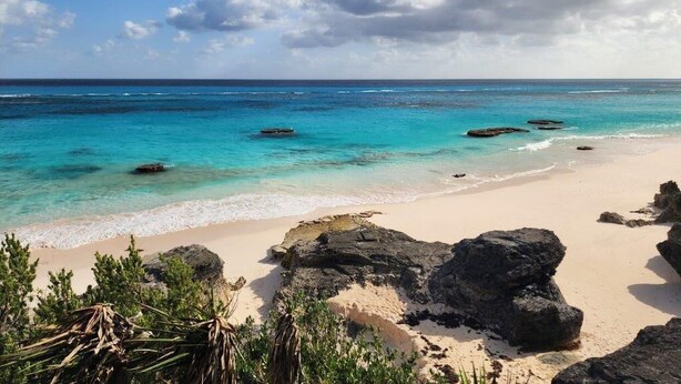 Ein Strand mit klarem türkisblauem Wasser, sandigem Ufer und großen Felsen.